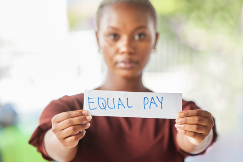 Woman holding up a written sign saying Equal Payl